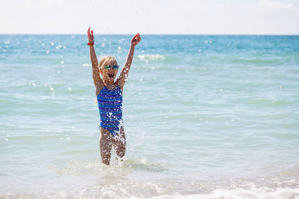 Kleine Mädchen spielen im Meer mit Wassertropfen und Wellen während des Familienurlaubs, glückliche aktive Kindheit - Foto, Bild