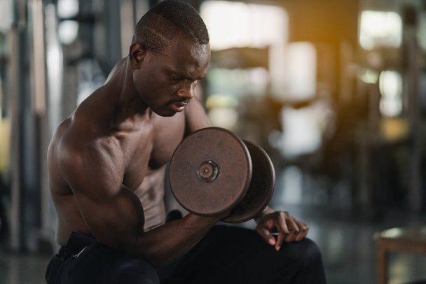 アフリカのスポーツマンの強い筋肉はジムのフィットネスルームでダンベルで体重の抜粋を動作します。ボディビルディングスポーツマンフィットネスコンセプト. - 写真・画像