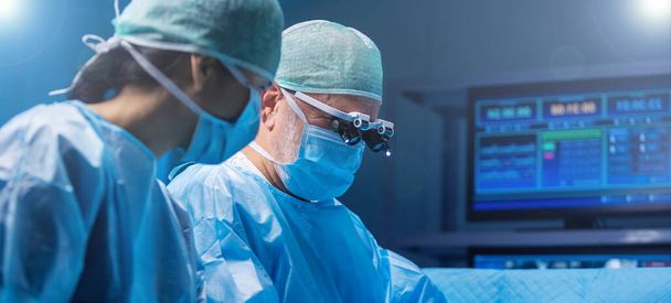 Diverse team of professional medical surgeons perform surgery in the operating room using high-tech equipment. Doctors work to save a patient in a modern hospital. The concept of medicine, technology - Photo, image