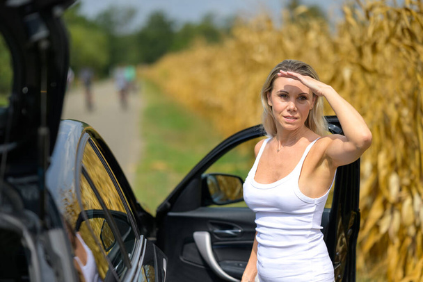 Kobieta stojąca przy samochodzie z przemyślanym wyglądem z powodu awarii samochodu czekając na pomoc z nią, aby podać do czoła - Zdjęcie, obraz