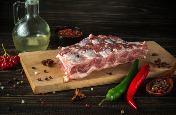 Fresh raw pork ribs on a kitchen cutting board with spices, oil and hot peppers. Cooking delicious food or grilling. - Photo, Image