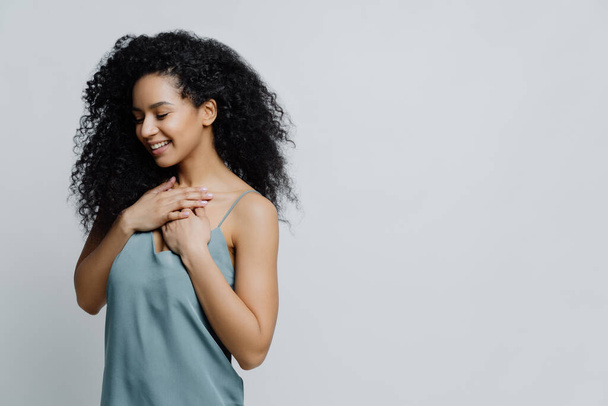 Profil álmodozó romantikus etnikai nő Afro frizura, hálóingben, tartja a kezét a mellkas, emlékeztet nagyon kellemes pillanat az életben mosolyog gyengéden csukott szemmel fejezi ki őszinte érzéseit - Fotó, kép