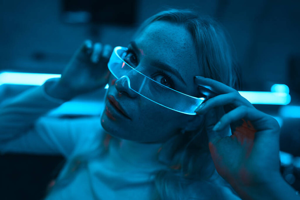 Neon blue light falls on a young woman wearing futuristic glass glasses. High quality photo - Foto, afbeelding