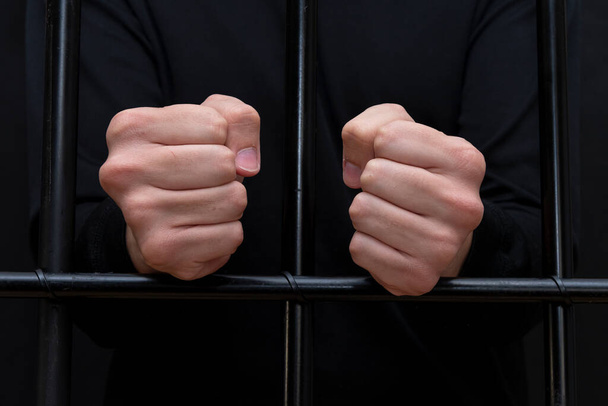 Κρατούμενος που κρατιέται χέρι χέρι σε γροθιές σε μπαρ του δικαστηρίου, σκοτεινός τόνος, επιλεκτική εστίαση.  - Φωτογραφία, εικόνα