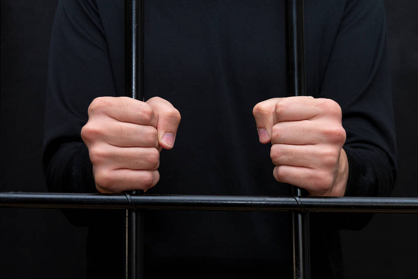 Więzień trzyma ręce za kratkami na sali sądowej, ciemny ton, selektywne skupienie.. - Zdjęcie, obraz