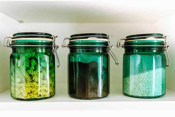 almacenamiento de productos en tarro de vidrio envasado ecológico. Tres frascos de vidrio verde con tapa de vidrio llena de productos a granel, cereales, arroz, pasta y café en el estante en fila - Foto, imagen