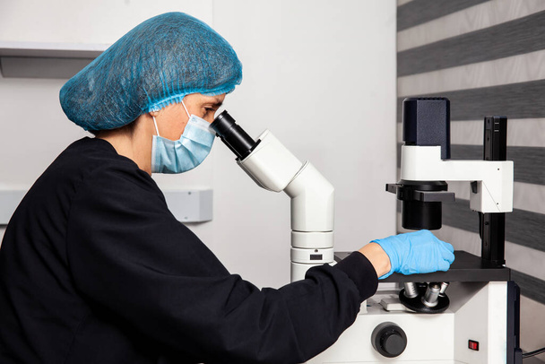 研究室で反転顕微鏡を使って患者のサンプルをスライドで見る女性科学者. - 写真・画像