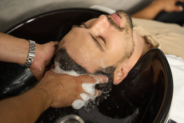 Cropped close-up shot of chill brunet man having his hair washed by a barbershop worker - Foto, Bild