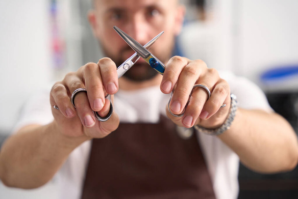 Selective focus photo of creative barber crossing two pairs of scissors while holding them in front of him - Фото, зображення