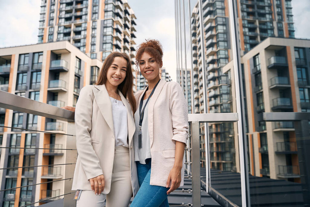 Joyous stylish young business ladies standing on office balcony and looking ahead - Foto, Bild