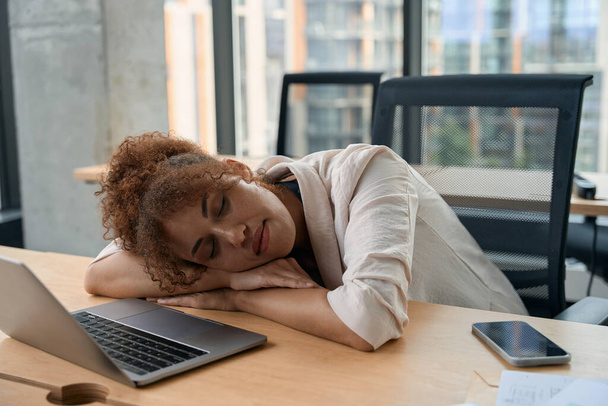 Exhausted young African American businesswoman sleeping on desk in her company office - 写真・画像