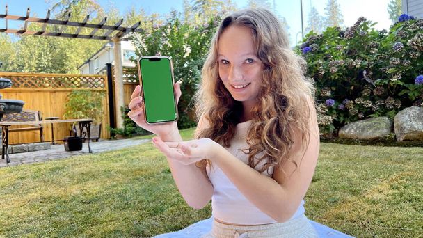 Блондинка-підліток дівчина з ключем від хроми На лузі у дворі Показує зелений екран фотоапарата Рекламний тренувальний додаток будь-якої соціальної мережі Ви можете побачити щастя і радість підлітка
 - Фото, зображення