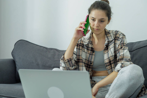 Vista frontal de una chica en un portátil sosteniendo un teléfono en sus manos. Comunicación en línea. Un trabajo moderno. Pantalla verde. Generación Z. Millennials - Foto, imagen