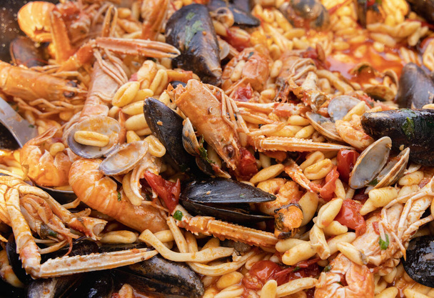 Italian Cavatelli allo scoglio, pasta with seafood and tomatoes close up in a frying pan. Mediterranean Apulian traditional food with fresh stewed clams, shrimps, mussels, octopus and squid - Photo, Image