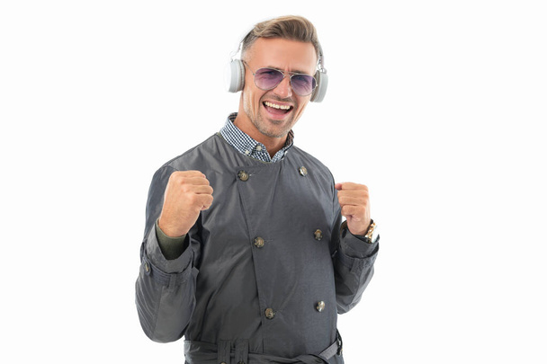 Happy guy celebrating with music making winning gesture, music. Businessman winner enjoying success listening to music in headphones studio isolated on white. - Фото, зображення
