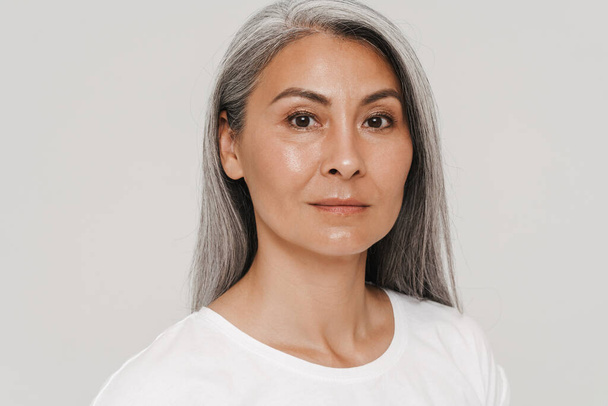 Mature asian woman with gray hair wearing t-shirt looking at camera isolated over white background - Фото, изображение