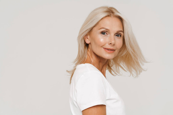 Mature blond happy woman wearing t-shirt smiling at camera isolated over white background - Valokuva, kuva