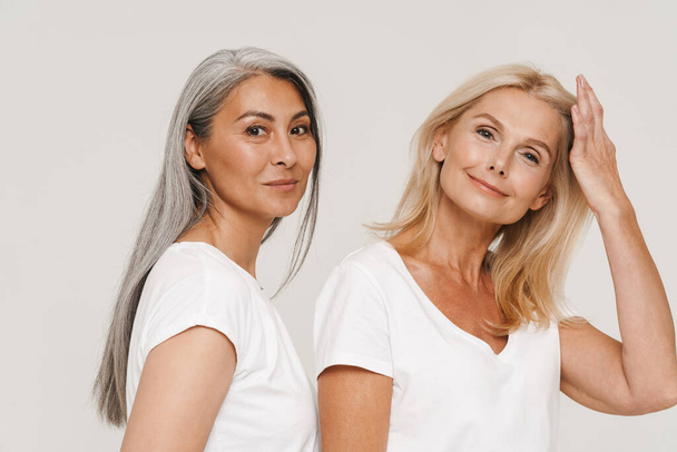 Mature multiracial women with gray hair wearing t-shirts posing at camera isolated over white background - Foto, Bild