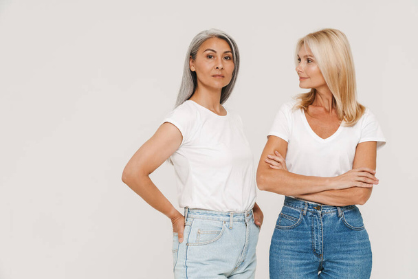 Mature multiracial women with gray hair wearing t-shirts posing at camera isolated over white background - Fotó, kép