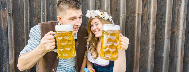 Young woman and man with beer glasses and pretzel on wooden background. Oktoberfest concept. - Photo, Image