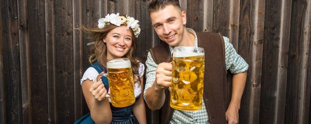 Young woman and man with beer glasses on wooden background. Oktoberfest concept. - 写真・画像