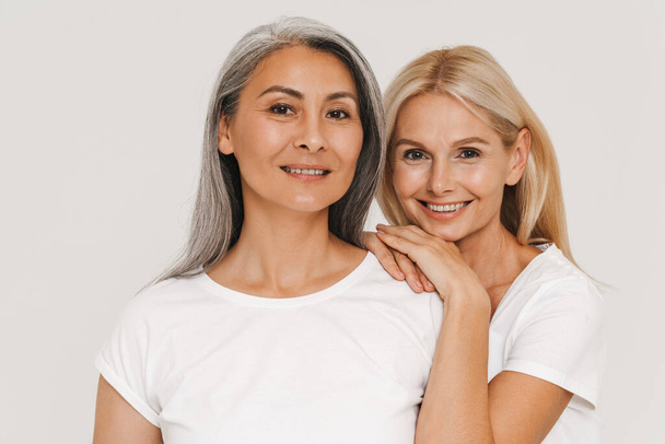 Mature multiracial women with gray hair wearing t-shirts smiling at camera isolated over white background - Valokuva, kuva