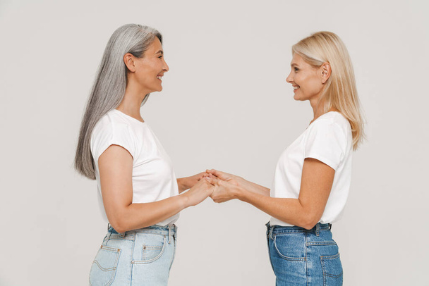 Mature multiracial women with gray hair wearing t-shirts posing at camera isolated over white background - Foto, immagini