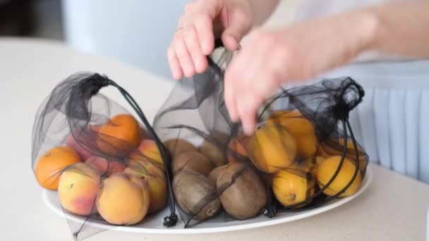 Eine junge Frau benutzt ein Bio-Fruchtnetz. Das Mädchen legt Äpfel und Orangen vom Tisch in das Essensraster. 4k-Video - Filmmaterial, Video
