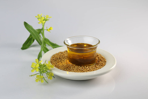 Studio shoot of mustard oil, seed and flower on dish on white background. useful in cooking and external body care. Mustard seeds and oil with mustard plants with pods and flowers - Photo, Image