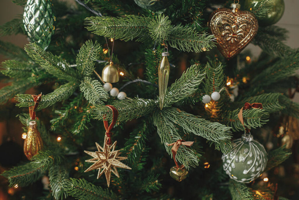 Árbol de Navidad con adornos vintage y luces doradas de cerca. Modernas ramas de árbol de Navidad decoradas con adornos elegantes en la habitación festiva. Vacaciones de invierno preparación, tiempo atmosférico - Foto, Imagen