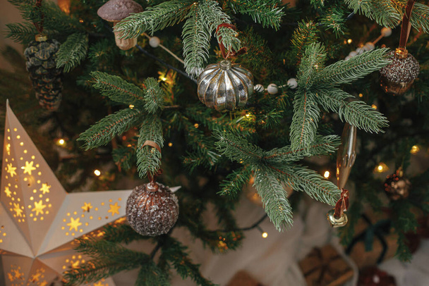 Christmas tree with vintage baubles and golden lights close up. Modern decorated christmas tree branches with stylish ornaments in festive room. Winter holidays preparation, atmospheric time - Photo, Image
