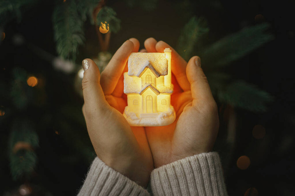 Kis izzó ház kezében a háttérben megvilágított karácsonyfa fények bokeh. Varázslatos ünnep. Kényelmes otthon. Légköri kép. Családi összetartás és biztonság koncepció. Boldog karácsonyt!! - Fotó, kép