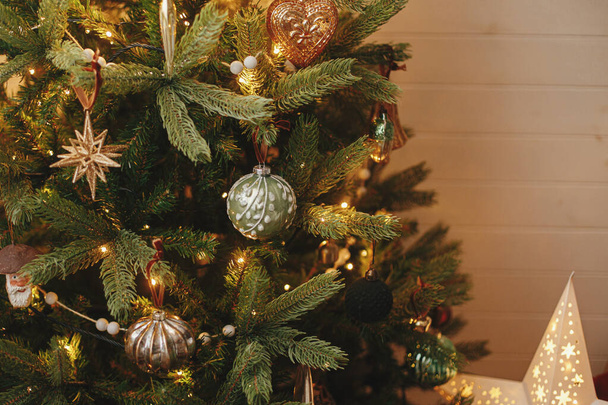 Albero di Natale con palline vintage e luci dorate da vicino. Moderni rami di albero di Natale decorati con eleganti ornamenti in camera festiva. Vacanze invernali, tempo atmosferico - Foto, immagini