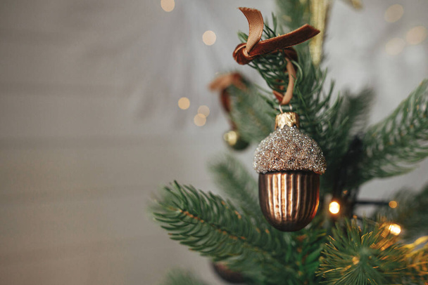 Árbol de Navidad con bellota vintage y adornos con luces doradas de cerca. Modernas ramas de árbol de Navidad decoradas con adornos elegantes en la habitación festiva. Vacaciones de invierno, tiempo atmosférico - Foto, Imagen