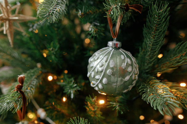 Árbol de Navidad con adornos vintage y luces doradas de cerca. Modernas ramas de árbol de Navidad decoradas con adornos elegantes en la habitación festiva. Vacaciones de invierno, tiempo atmosférico - Foto, Imagen