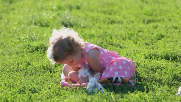 A little girl is playing with a real rabbit in the garden. Child and rabbit. Easter holidays. Baby feeding of pets. Fluffy pet - Footage, Video