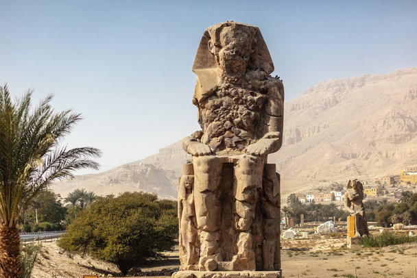 Дневной вид на колоссы Мемнона. Две большие каменные фигуры с изображением сидящего фараона. Это все, что осталось от огромного храма памяти Аменхотепа III. - Фото, изображение