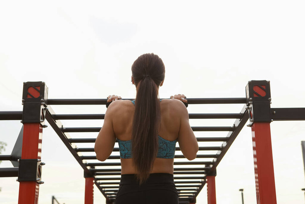 Matala kulma taaksepäin kuva urheilullinen nainen tekee pull ups vaakasuorassa tikkaat ulkona - Valokuva, kuva