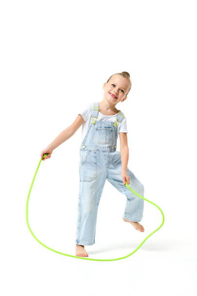 Porträt eines kleinen Mädchens in Jeans-Overalls mit Springseil auf weißem Hintergrund. - Foto, Bild