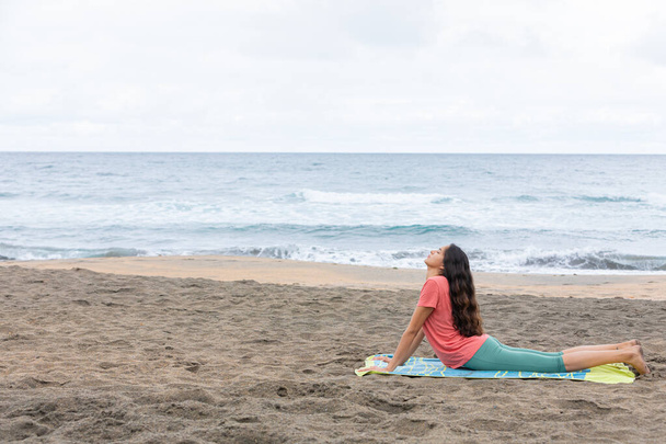 Tranquilla signora ispanica praticare Bhujangasana yoga posa sulla spiaggia sabbiosa  - Foto, immagini