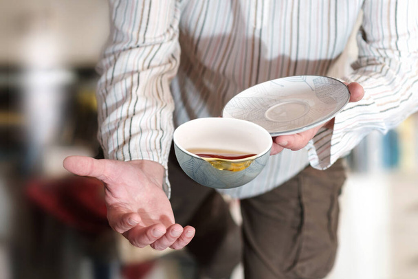 A man in sripy shirt dropping teacup with tea, selective focus - Fotografie, Obrázek