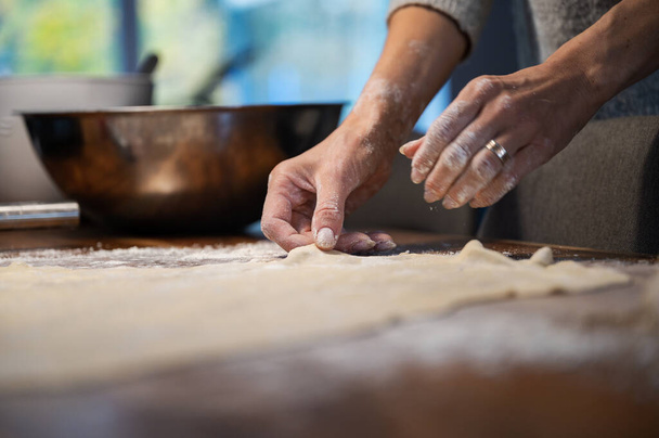 Niedrige Ansicht einer Frau, die hausgemachten Teig für einen Strudel oder Kuchen zubereitet und ihn auf einem mit Mehl bestäubten Holztisch platziert. - Foto, Bild