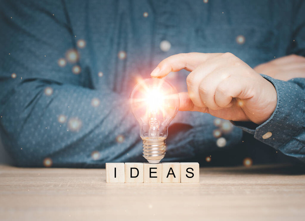 koncept inovace Inspirace k inovaci moderní technologické komunikace prostřednictvím nápadů Ruka vynálezce drží žárovku na dřevěném bloku s písmeny nápadu - Fotografie, Obrázek