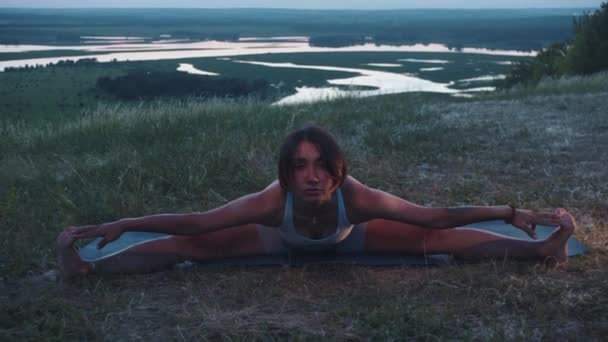 Egy vékony nő ül a hasadékon egy hegyen egy jóga szőnyegen, és előrehajol. Középső felvétel - Felvétel, videó