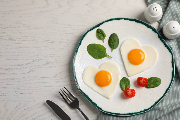 Heart shaped fried eggs served on white wooden table, flat lay. Space for text - Foto, Bild