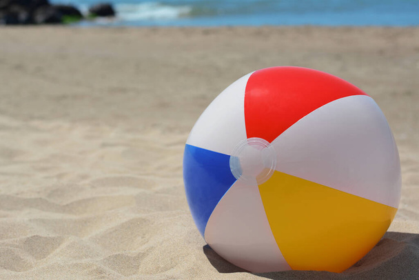 Colorful beach ball on sand near sea, space for text - Фото, зображення
