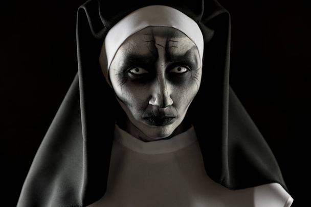 Portrait of scary devilish nun on black background. Halloween party look - Фото, изображение