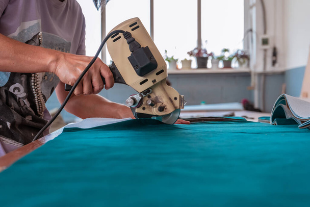 The cutter cuts the fabric with a disc knife in a sewing workshop - Fotografie, Obrázek