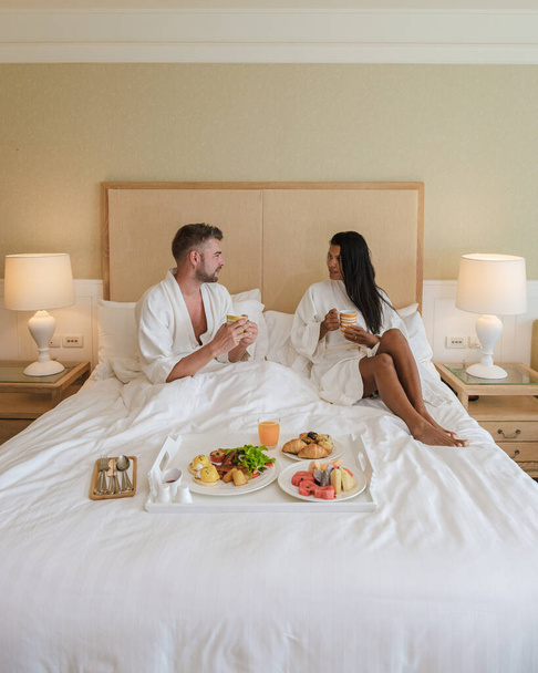 ベッドで朝食をとる夫婦とベッドルームで朝食をとる男女。コーヒーとフルーツで - 写真・画像