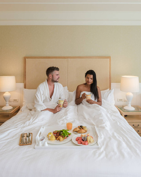Çift yatakta kahvaltı yapıyor, erkek ve kadın yatak odasında sabah kahvaltı yapıyor. Kahve ve meyve ile. - Fotoğraf, Görsel